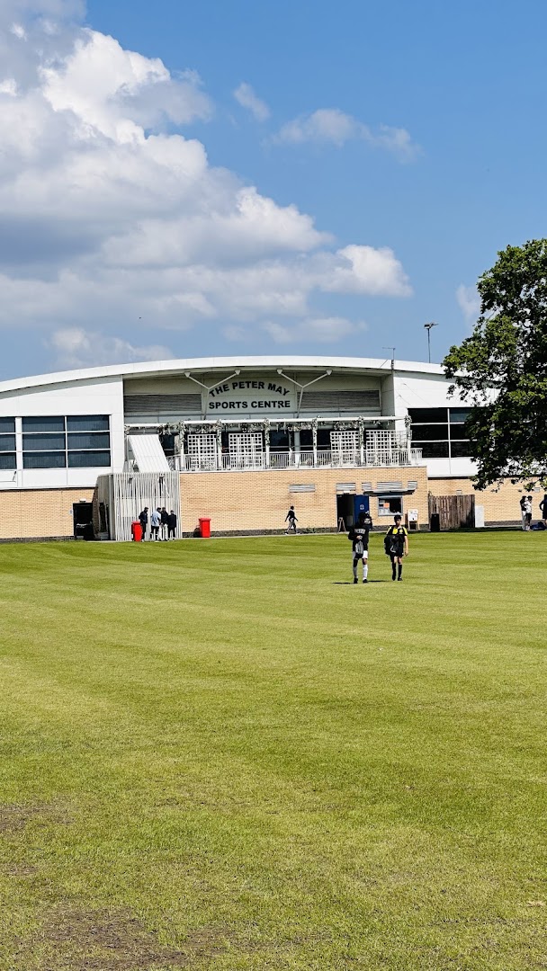Exterior view of Peter May Sports Centre with green fields and families enjoying activities